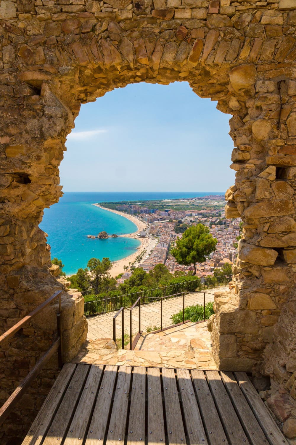 Vue panoramique de la plage de Blanes à travers une porte en pierre du château San Juan